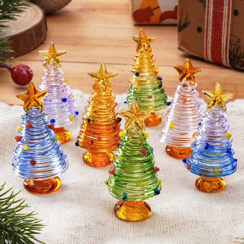 May include: A collection of seven miniature glass Christmas trees in various colors including blue, purple, orange, green, and clear. Each tree features a spiral design with small colored glass dots and a gold star topper on a base.