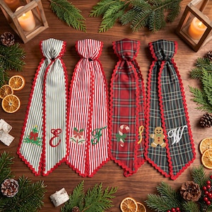 Puede incluir: Cuatro cintas largas de tela con bordes festoneados rojos, con patrones festivos que incluyen rayas grises, rayas rojas, cuadros rojos y cuadros verde oscuro. Cada cinta muestra iconos navideños y letras bordadas: un árbol, E, campanas, F, un bastón de caramelo, S, un hombre de jengibre y W.