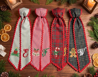 May include: Four long fabric ribbons with scalloped red edges, featuring festive patterns including grey stripes, red stripes, red plaid, and dark green plaid. Each ribbon displays embroidered holiday icons and letters: a tree, E, bells, F, candy cane, S, gingerbread man, and W.