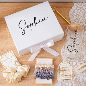 Peut inclure: Une bo&icirc;te cadeau blanche avec le nom "Sophia" en &eacute;criture cursive, un bocal en verre avec un couvercle en bois et le nom "Sophia", et divers accessoires pour cheveux. Les accessoires comprennent des chouchous et des pinces &agrave; cheveux. Les articles sont dispos&eacute;s sur une surface en bois.