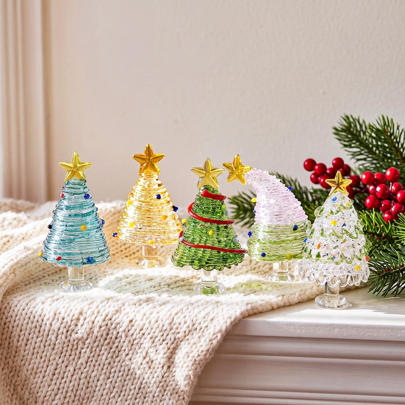 May include: Five miniature glass Christmas trees in various colors including light blue, yellow, green, pink, and clear. Each tree features a coiled glass design, small colorful glass bead accents, and a gold-toned star topper.