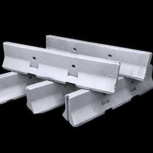 May include: A stack of three white concrete traffic barriers featuring a low-profile design with a wide base, a sloped front face, and a vertical top section. Each barrier includes two circular holes positioned horizontally along the upper edge.