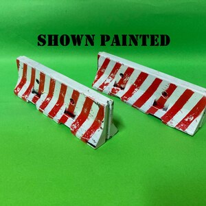 May include: Two miniature road barriers featuring a white base with diagonal red stripes. The barriers have a textured, weathered appearance and include the text SHOWN PAINTED in black letters above them on the green background.