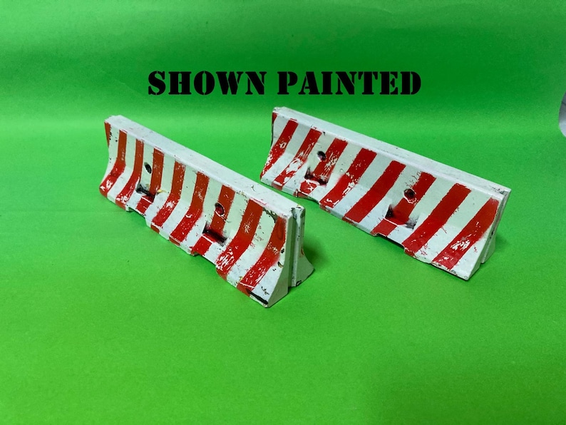 May include: Two miniature road barriers featuring a white base with diagonal red stripes. The barriers have a textured, weathered appearance and include the text SHOWN PAINTED in black letters above them on the green background.