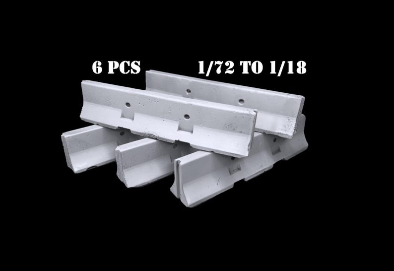 May include: A set of 6 white concrete-style jersey barriers featuring a sloped profile and two circular holes along the top edge. The text 6 PCS and 1/72 TO 1/18 is printed in white above the barriers, which are arranged in a stacked formation.