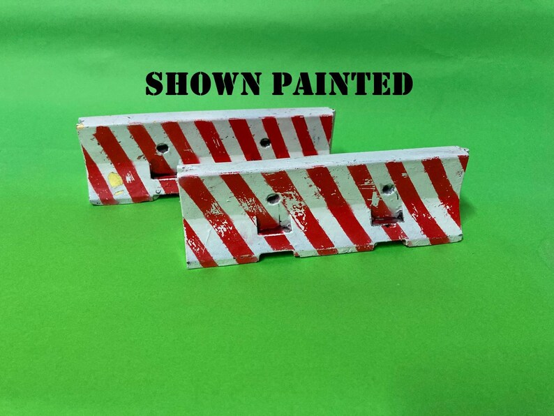 May include: Two miniature concrete-style traffic barriers featuring diagonal red and white hazard stripes. The barriers have a weathered, distressed finish with visible paint chips. The text SHOWN PAINTED is printed in black above the objects.