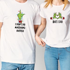 Op de afbeelding: Twee witte T-shirts met bijpassende afbeeldingen. Eén shirt heeft een groene hand die de middelvinger opsteekt met de tekst "I DON'T DO MATCHING OUTFITS". Het andere shirt heeft groene handen die een hart vormen met de tekst "BUT I DO".