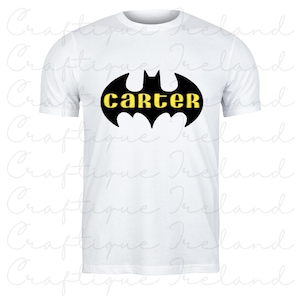 Op de afbeelding: Wit T-shirt met een zwart vleermuissymbool en de naam "CARTER" in geel. Het ontwerp is gedrukt op de voorkant van het T-shirt met korte mouwen. Het T-shirt is gemaakt van een zacht, comfortabel materiaal.