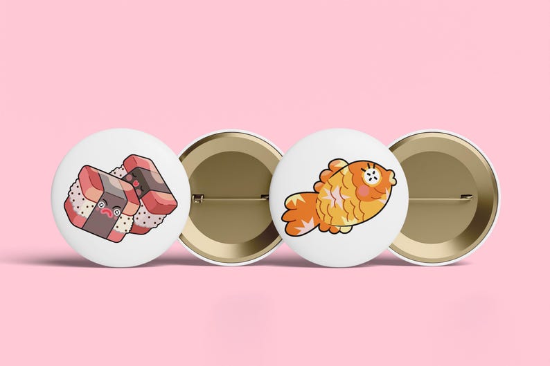 May include: Two circular pin-back buttons with white backgrounds. One button features a cartoon illustration of two pieces of sushi with faces, and the other button displays a cartoon illustration of a golden orange fish with a surprised expression.