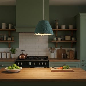 Puede incluir: Una cocina con paredes verdes, estanterías de madera y una isla de bloque de carnicero. Una lámpara colgante turquesa cuelga sobre la isla. Un cuenco de manzanas verdes está sobre la isla y una tabla de cortar con verduras está cerca.