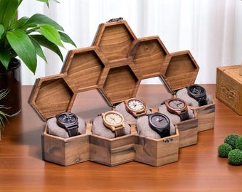 May include: A wooden watch display case in a honeycomb design, holding six watches. The case is open, revealing the watches on gray cushions. The watches have various band and face colors, including black, brown, and beige.