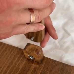 May include: Wooden furniture assembly in progress. A person is using a tool to connect two wooden pieces. The pieces are a warm brown color, and the tool is also wooden. The background is a soft, white fabric.