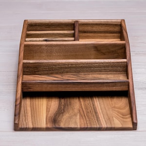 May include: A wooden desk organizer with multiple compartments. The organizer is made of a dark brown wood and has a sloped design. It features several sections for storing items like pens, papers, and other office supplies.