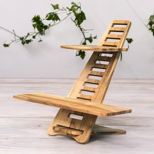 Puede incluir: Un soporte de madera para portátil con un diseño ergonómico único. El soporte está hecho de madera de color claro y presenta una parte trasera con listones, un estante pequeño y una base más grande. El soporte está diseñado para elevar un portátil para un uso cómodo. El soporte mide aproximadamente 51 cm de altura.