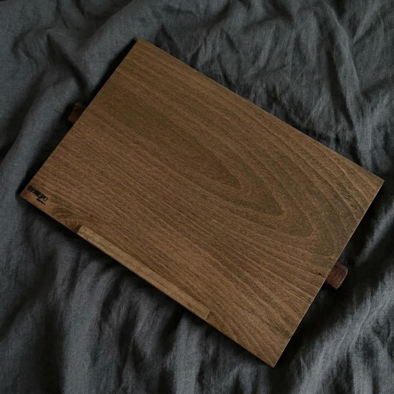 May include: A rectangular wooden book stand with a rich brown finish. The stand features a small ledge to hold pages and a support piece. The wood grain is visible. The word "REMEDIO" is printed on the stand.