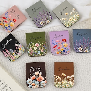 Peut inclure: Une collection de neuf marque-pages magnétiques rectangulaires de différentes couleurs, notamment rose, gris, noir, vert olive, violet, bleu et marron. Chaque marque-page présente un imprimé floral unique et un nom imprimé : Dorothy, Karen, Gemma, Candice, Angela, Lauren, Regina, Mandy et Zenobia.