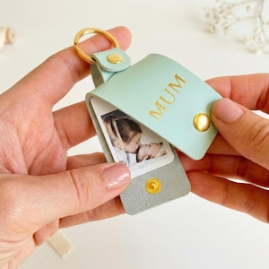 May include: A mint green leather keychain with a gold-colored keyring and snap closure. The keychain has the word "MUM" in gold lettering and holds a small photograph. A thoughtful gift.