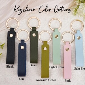 May include: A selection of leather keychains in various colors, including black, blue, green, avocado green, light green, pink, and light blue. Each keychain has a gold-colored ring and a matching snap closure. The text "Keychain Color Options" is at the top.
