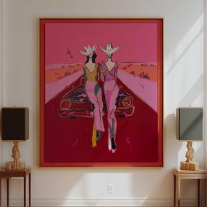 Peut inclure: Une grande œuvre d'art encadrée représente deux personnages en chapeaux de cow-boy, assis sur une voiture sur une route rouge. L'œuvre est dans les tons de rose, de rouge et d'orange. Deux lampes avec des bases en bois et des abat-jours foncés encadrent l'œuvre, posées sur de petites tables en bois.