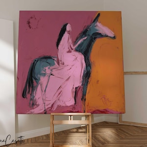 May include: An abstract painting on canvas depicts a figure on horseback. The artwork features a pink-clad rider on a dark blue horse against a backdrop of pink and orange hues. The painting is displayed on a wooden easel.