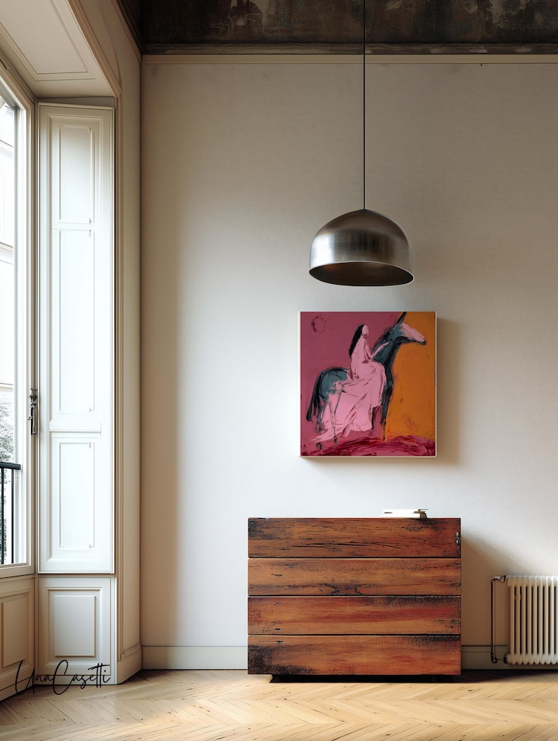May include: An abstract painting of a figure on a horse in pink and blue hangs above a wooden chest of drawers. The room has a large window with white shutters and a silver pendant light.