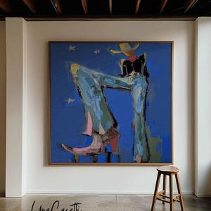 May include: A large square painting in a wooden frame featuring an abstract figure wearing a cowboy hat, a black top, and light blue flared trousers with pink boots against a deep blue background with small white stars and the text Una Casetti.