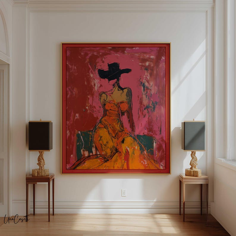 May include: An abstract painting of a figure in an orange dress and black hat against a red and pink background. The artwork is framed in red and hangs on a white wall. Two lamps with black shades and wooden bases flank the painting.