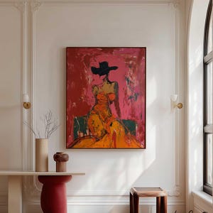 May include: Abstract painting of a figure in an orange dress and black hat against a red and pink background. The artwork is framed in a dark brown frame. The room features a console table, a red pedestal, and a wooden stool.
