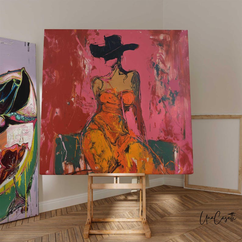 May include: Abstract painting of a woman in an orange dress and black hat, set against a red and pink background. The artwork is displayed on a wooden easel in a room with hardwood floors. The artist's signature is visible.