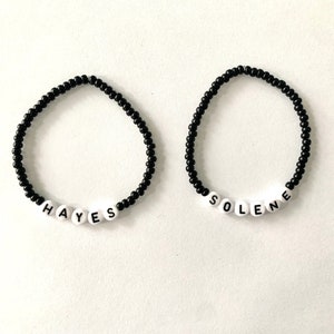 May include: Two black beaded bracelets with white letter beads spelling out the names "HAYES" and "SOLENE".