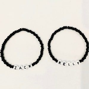 May include: Two black beaded bracelets with white letter beads spelling out the names "Zack" and "Kelly".