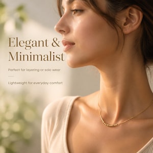 Puede incluir: Un collar de cadena en tono dorado que presenta una serie de pequeñas cuentas cilíndricas y esféricas en el centro. El texto en la imagen dice: Elegant & Minimalist, Perfect for layering or solo wear, Lightweight for everyday comfort.