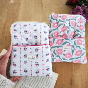 Peut inclure: Deux pochettes à motifs floraux avec fermetures éclair dorées. L'une présente un fond blanc avec un motif matelassé et de petites fleurs rouges et bleues. L'autre a un motif floral rose sur fond blanc.
