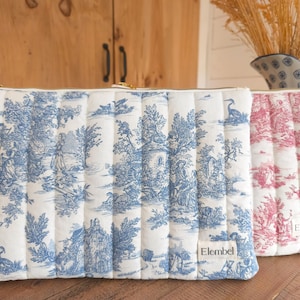 Può includere: Due trousse trapuntate con cerniere dorate. Una borsa è bianca con scene toile de Jouy blu, l'altra è bianca con scene toile de Jouy rosa. Le borse sono rettangolari con cuciture verticali e una piccola etichetta "Elembel".