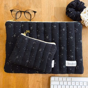 May include: A black quilted pouch and a matching larger black quilted sleeve, both featuring a white speckled pattern and gold zipper pulls. The larger sleeve has a white label with the text Elembel. Also included are black glasses and a black scrunchie.