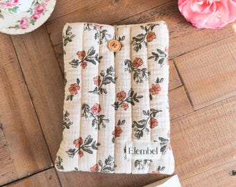 May include: A rectangular, quilted fabric pouch in an off-white color featuring a repeating pattern of small orange flowers and green leaves. The pouch includes a single wooden button closure at the top and a white fabric label reading Elembel.
