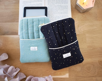 May include: Two quilted fabric sleeves for e-readers, one in sage green and one in navy blue, both featuring gold star patterns and a white label with the text Elembe. Each sleeve has a zippered top closure with a crescent moon charm pull.