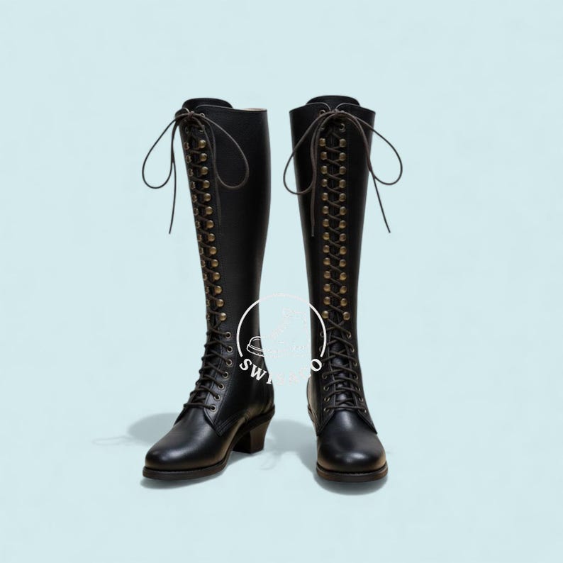 K&ouml;nnte beinhalten: Ein Paar schwarze kniehohe Stiefel mit Schn&uuml;rdesign. Die Stiefel haben eine Reihe von &Ouml;sen mit Schn&uuml;rsenkeln und einen kleinen Absatz. Die Stiefel sind aus gl&auml;nzendem Material und vor hellblauem Hintergrund.