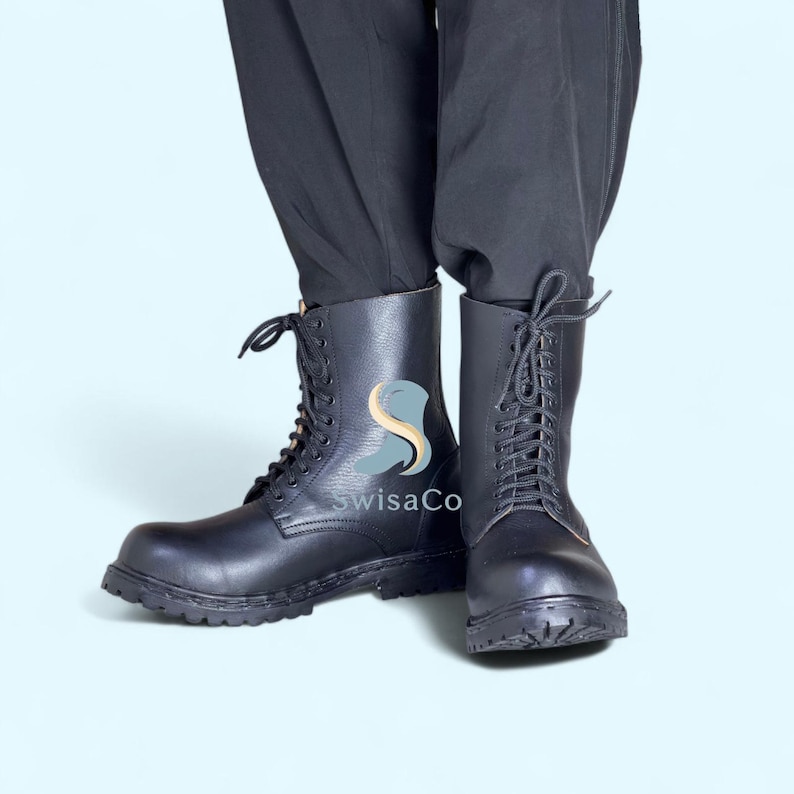 Pode incluir: Botas de combate de couro preto com design de atacadores. As botas t&ecirc;m uma sola resistente e s&atilde;o de altura m&eacute;dia. As botas s&atilde;o mostradas em um fundo azul claro. O texto "swisaCo" &eacute; vis&iacute;vel na lateral das botas.
