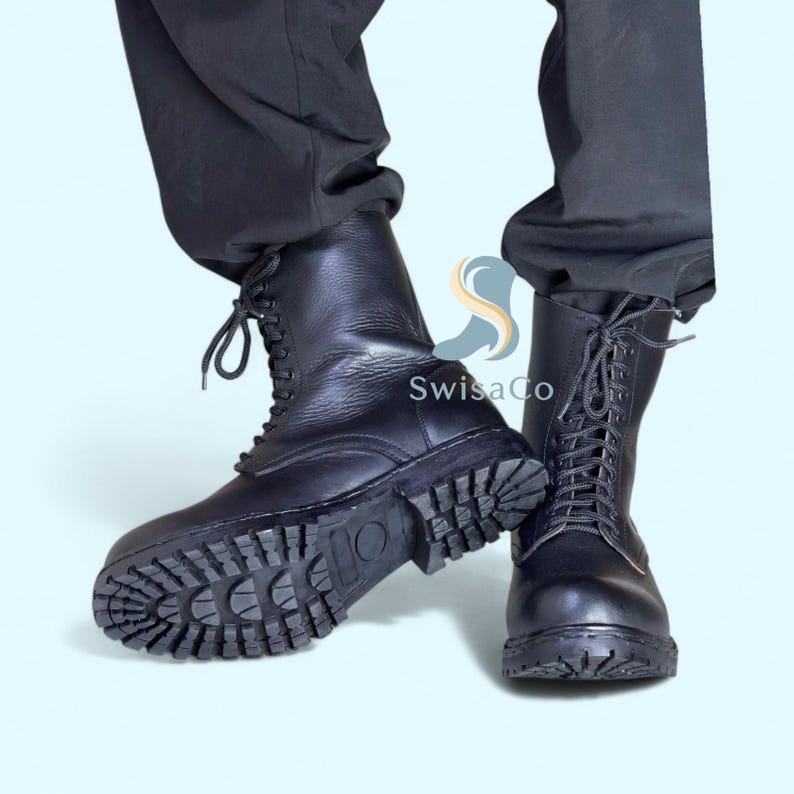 Pode incluir: Botas de combate de couro preto com solas grossas e com ranhuras e fechos de atacadores. As botas t&ecirc;m um design de cano alto e s&atilde;o usadas com cal&ccedil;as pretas. As botas s&atilde;o resistentes e parecem dur&aacute;veis.