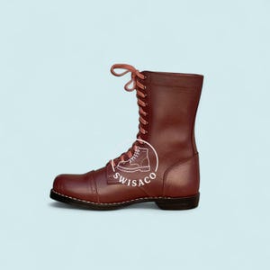 May include: A burgundy leather boot with a high shaft and lace-up fastening. The boot features a cap toe and a stitched sole. The brand logo "SWISACO" is visible on the side. The boot is set against a light blue background.