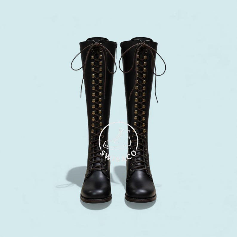 K&ouml;nnte beinhalten: Ein Paar schwarze kniehohe Stiefel mit Schn&uuml;rdesign und Messing&ouml;sen. Die Stiefel haben eine runde Spitze und einen braunen Schn&uuml;rverschluss. Die Stiefel werden vor einem hellblauen Hintergrund pr&auml;sentiert.
