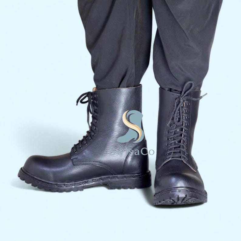 Pode incluir: Botas de combate em couro preto com design de atacadores. As botas t&ecirc;m uma sola resistente e um design de cano alto. As botas s&atilde;o mostradas dos tornozelos para baixo, com o utilizador em cal&ccedil;as pretas. As botas s&atilde;o um estilo cl&aacute;ssico.