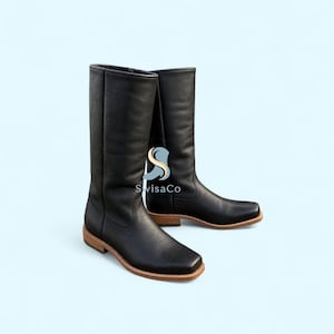 Könnte beinhalten: Ein Paar wadenhohe Stiefel aus schwarzem Leder mit quadratischer Zehenpartie, glatter matter Oberfläche sowie einem Absatz und einer Sohle aus hellbraunem Schichtholz. Die Stiefel tragen den Schriftzug SwisaCo in stilisierter Schrift am Schaft.