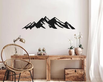 May include: Black metal mountain range wall art. The artwork depicts a stylized mountain range silhouette, suitable for home or office decor. The piece is mounted on a white wall, above a wooden desk and chair.