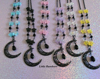 May include: A collection of celestial-themed necklaces. Each necklace features a black filigree crescent moon pendant with a dangling black teardrop bead. The chains are adorned with star or butterfly-shaped beads in various colors, including blue, pink, and yellow.