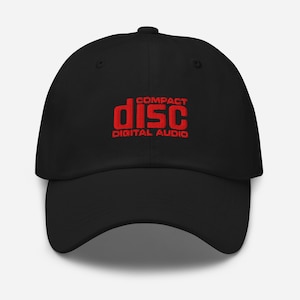 Può includere: Cappellino da baseball nero con la scritta rossa "COMPACT DISC DIGITAL AUDIO" ricamata sul davanti. Il cappellino ha una visiera curva e un bottone sulla parte superiore. Un accessorio classico e casual.