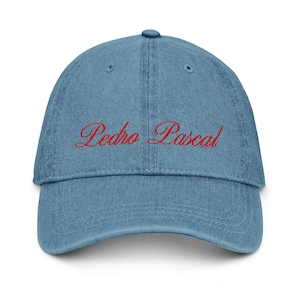 Peut inclure: Casquette de baseball en jean bleu clair avec une visière incurvée. Le texte rouge brodé "Pedro Pascal" est arqué sur le devant. La casquette a un bouton sur le dessus et une sangle réglable.