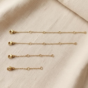 Può includere: Quattro estensori di catena color oro con chiusure a moschettone. Ogni estensore ha una catena delicata con piccoli anelli circolari e un anello all'estremità. Gli estensori variano in lunghezza, perfetti per gioielli.