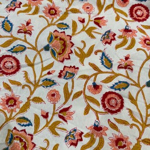 May include: White fabric with a repeating floral pattern. The design features red, peach, and blue flowers with yellow-gold stems and leaves. The flowers are detailed with multiple layers of petals.